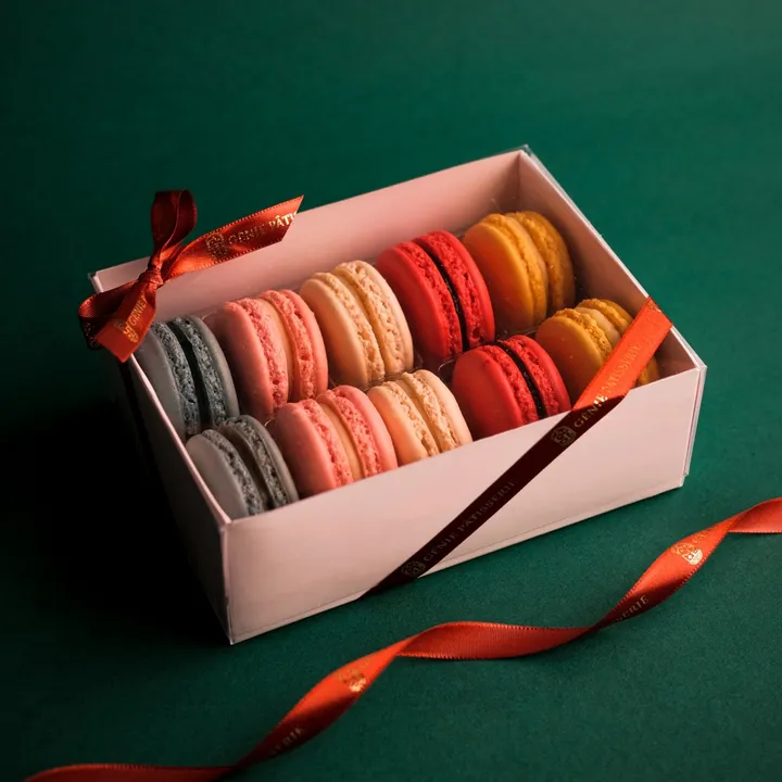 Caixa de presente Génie aberta, com macarons coloridos e fita vermelha.